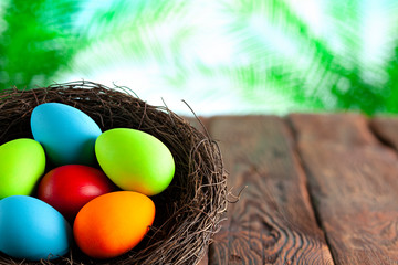 Colored Easter eggs in the nest on wooden table and nature background