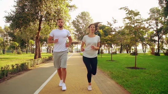 happy friends jogging in city park enjoy healthy lifestyle young woman with blond hair wearing leggings handsome man shod white sneakers summer time outdoors