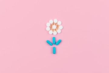 Bright blue and white pills and tablets in flower shape on pink background. Medicines, drugs, pharmacy concept. Flat lay, top view, minimal style