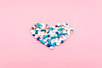 Fototapeta premium Bright blue and white pills and tablets in heart shape on pink background. Medicines, drugs, pharmacy concept. Flat lay, top view, minimal style