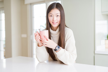 Beautiful Asian woman drinking a cup of coffee with a happy face standing and smiling with a confident smile showing teeth