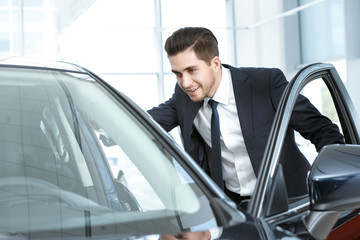 Plakat Taking a look. Half length portrait of a smiling businessman looking inside the car through the open door