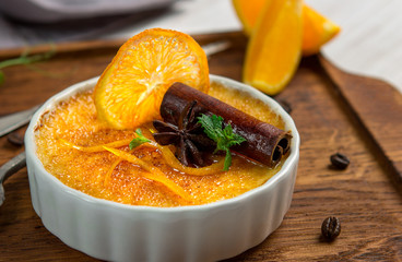 Orange creme brulee dessert in white bowl with cinnamon and mint on wooden background, close up