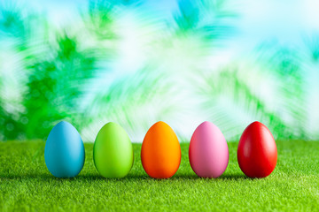 Five colored Easter eggs on short cut grass and abstract nature background