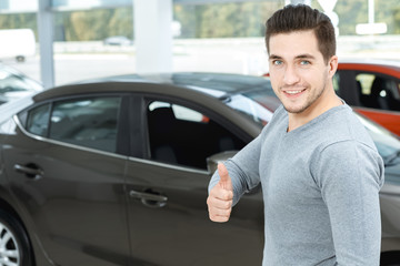 Happy car owner. Half length portrait of a handsome man smiling happily and showing thumbs up in a car salon