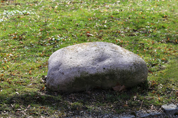 A large round stone lies in the park on the grass