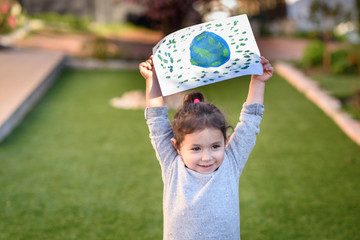 Portrait of the cute little girl holding the drawing earth globe outdoor sunny day. Child painting a picture of earth.Earth day, plastic free and zero waste concept.