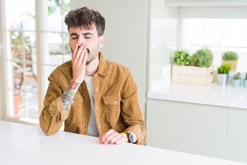 Naklejka premium Young man wearing casual jacket sitting on white table bored yawning tired covering mouth with hand. Restless and sleepiness.