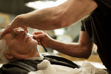 Barber shaves senior man's face with a straight razor