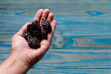 Female left hand holding prune on blue pinus wood.
