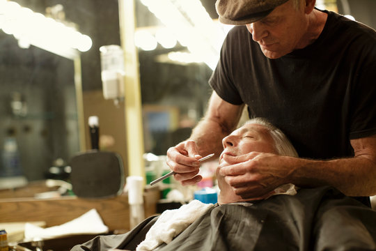 Barber uses a straight razor to shave senior man's face