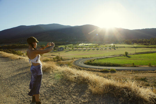 Young woman taking photo of rural landscape with her smartphone