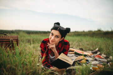 Woman with book lies on plaid, picnic in field