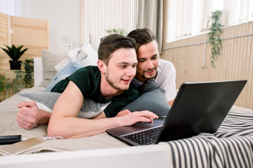 Modern technology. Pretty young gay couple using laptop while posing on bed and spending time together