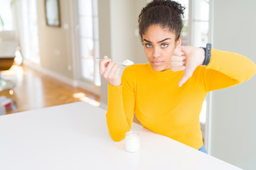 Fototapeta na wymiar Young african american woman eating a healthy natural yogurt with angry face, negative sign showing dislike with thumbs down, rejection concept