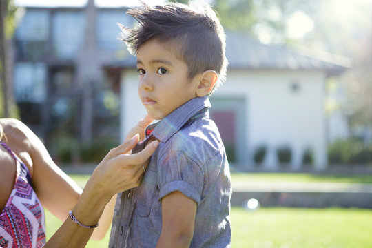 Young boy looks off while mother buttons his shirt
