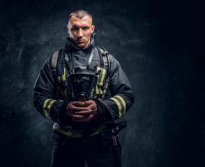A handsome fireman wearing protective uniform holding an oxygen mask and looking at a camera....