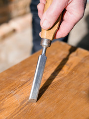 carpenter with chisel in the hands on the workbench in carpentry, close up carpenter's hands that work with cutter