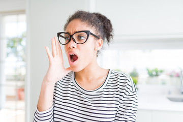 Beautiful young african american woman with afro hair wearing glasses shouting and screaming loud to side with hand on mouth. Communication concept.