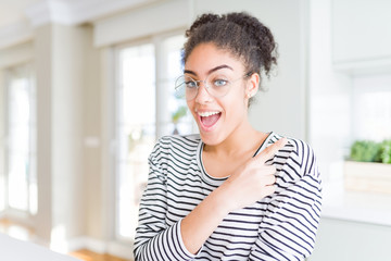 Beautiful young african american woman with afro hair wearing glasses cheerful with a smile of face pointing with hand and finger up to the side with happy and natural expression on face