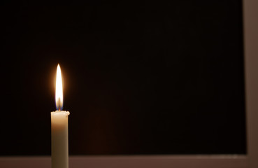 White burning candle on a black background. Mourning, burning candle.