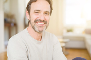 Handsome middle age man sitting on the floor smiling at the camera at home