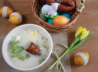 Śniadanie wielkanocne - żurek z jajkiemi i kiełbasą, obok pisanki, koszyczek ze świeconką