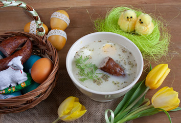 Śniadanie wielkanocne - żurek z jajkiemi i kiełbasą, obok pisanki, koszyczek ze świeconką
