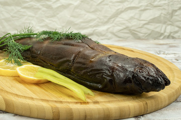 Smoked fish slice decorated with lemon, pepper and dill on a round wooden board