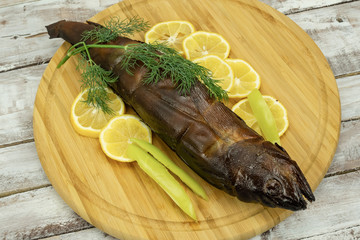 Smoked fish, decorated with lemon, pepper and dill on a round wooden board