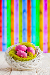 Easter eggs in the nest and wooden table on colorful background