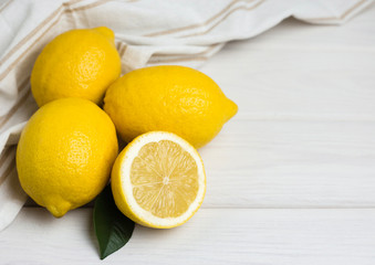 Whole and sliced lemons with fabric on white wooden background. Organic fresh citrus fruits, top view, copy space.
