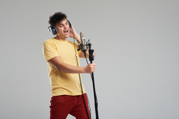 Portrait of rock singer man in studio professional headphones keeping static acoustic mic, sings a...