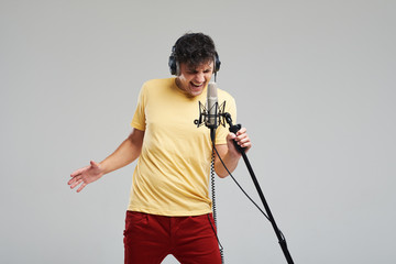 Portrait of rock singer man in studio professional headphones keeping static acoustic mic, sings a...