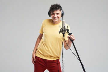 Portrait of rock singer man in studio professional headphones keeping static acoustic mic, sings a...