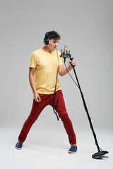 Portrait of rock singer man in studio professional headphones keeping static acoustic mic, sings a...