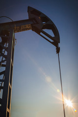Oil pump on the background of blue sky and the morning sun, sun glare on the oil pump