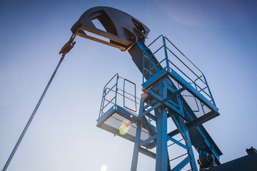 Oil pump on the background of blue sky and the morning sun, sun glare on the oil pump