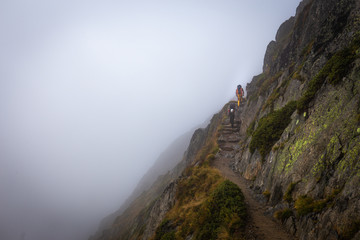 Two backpackers walking mountain cliff trail.