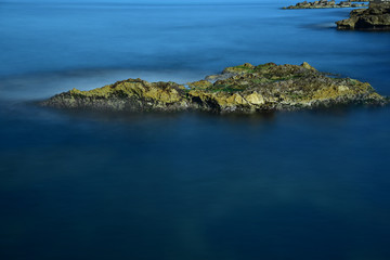 langzeitaufnahme eines felsens in blauem ruhigem wasser