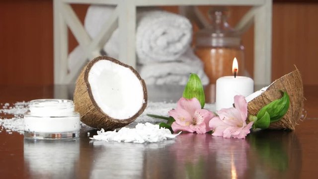 Burning candle, half of coconut , flakes of coconut, cream in a glass cup, pink flowers  are lying on a black  table against the background of the accessories  and cosmetics for spa treatments and aro