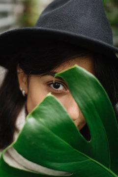 Portrait of woman wearing hat peeping through leaf