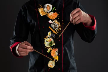 Foto auf Acrylglas Sushi-bar Meisterkoch hält Stäbchen mit fliegendem Sushi