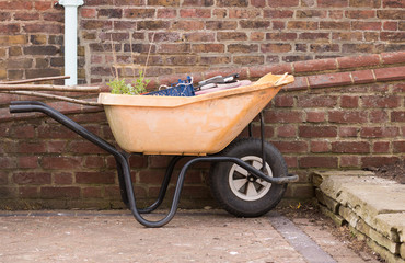 Close-up: Old Orange Garden Carts with Garden Tools and Green Plant are Near Brick Wall. Spring Garden Works. A gardener's cart. Concept: Gardening and Agriculture.