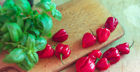 Red small paprikas on wooden cutting board. Basil leaves on the side.
