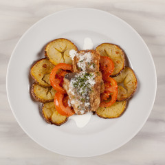 Baked potatoes in the peel sliced with tomato and grilled meat in a white sauce.