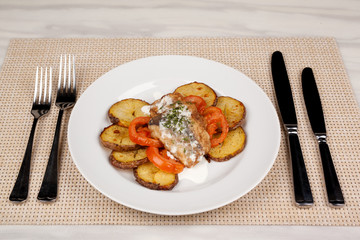 Baked potatoes in the peel sliced with tomato and grilled meat in a white sauce.