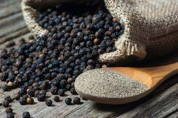 heap of black pepper and black pepper powder in wooden spoon, milled peppercorns on wooden...