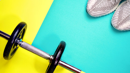 Fitness equipment on yellow and blue color background. Healthy and active lifestyle concept with trendy sneakers, dumbbell. Copy space, flat lay, top view