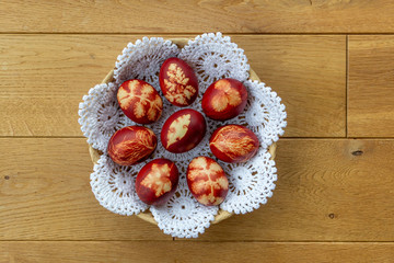 Easter eggs dyed with onion peels with a pattern of plants and leaves in a basket on a white lace...